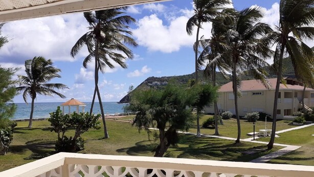 Uitzicht vanaf een balkon op een strand met palmbomen, een prieel en een gebouw met een rood dak.