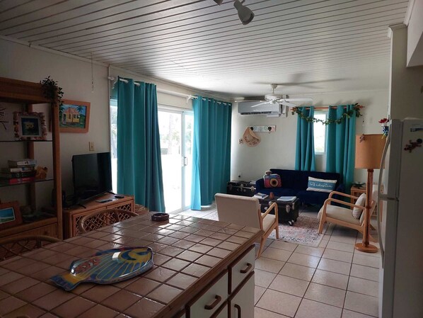 Een gezellige woonkamer met een betegelde vloer, een televisie, een bank en een eethoek met een tafel en stoelen.