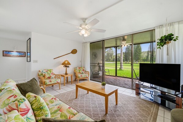 Ein Wohnzimmer mit Sofa, Sesseln, Couchtisch, Fernseher und Deckenventilator.
