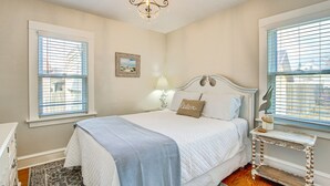 Un dormitorio con cama, mesita de noche, lámpara, candelabro y ventana con persianas.