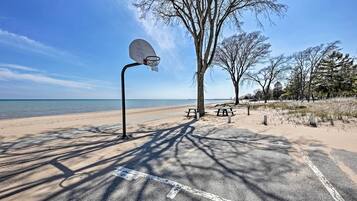Una pista de bàsquet amb cèrcol, taules de pícnic i arbres a prop d'una platja.