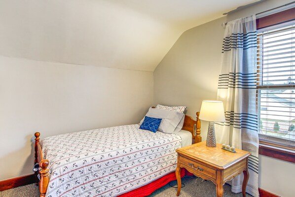 Un dormitorio con cama, mesita de noche con lámpara y ventana con cortinas.