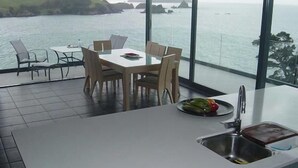 A modern kitchen with a large island, dining area with chairs, and a view of the sea.