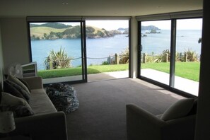 A room with a large sliding glass door leading to a scenic view of the sea and hills.