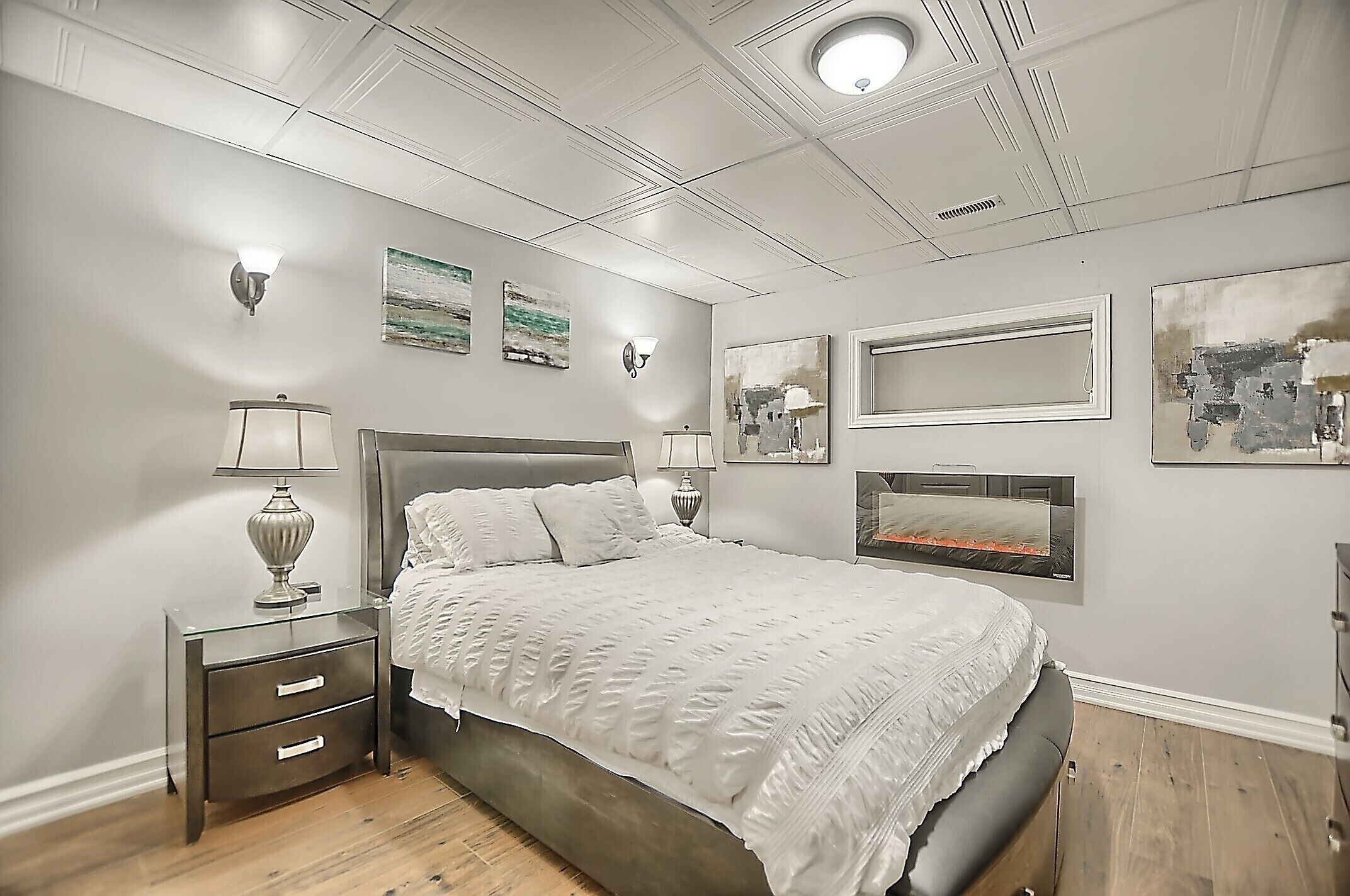 A bedroom with a large bed, a nightstand with drawers, a wall-mounted TV, and artwork on the walls.