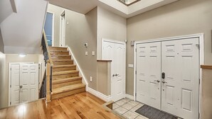 Um corredor amplo com piso de madeira, uma escada e um conjunto de portas duplas.