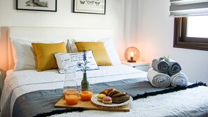 A neatly made bed with a white and gray bedspread, two mustard-colored pillows, and a bedside table with a lamp and a framed picture. - Phaedrus Living: Seaside Luxury Flat Lighthouse 53 (Paphos)