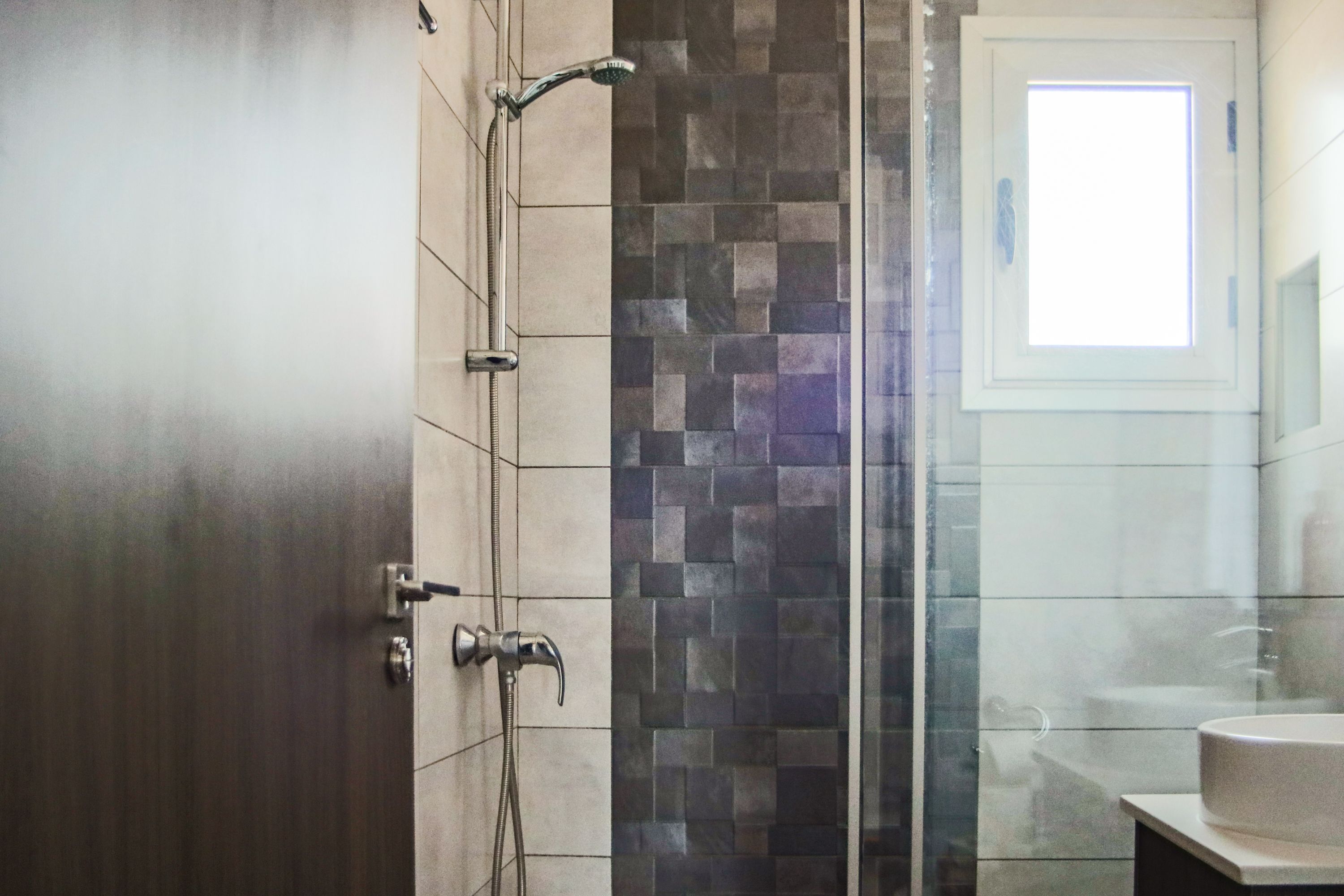 A bathroom with a shower, tiled walls, a sink, and a window.