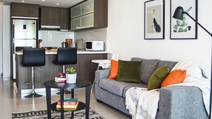 A modern living room with a grey sofa, two black bar stools, a small round table with a plant, and a white coffee table. - Phaedrus Living: Seaside Luxury Flat Lighthouse 53 (Paphos)