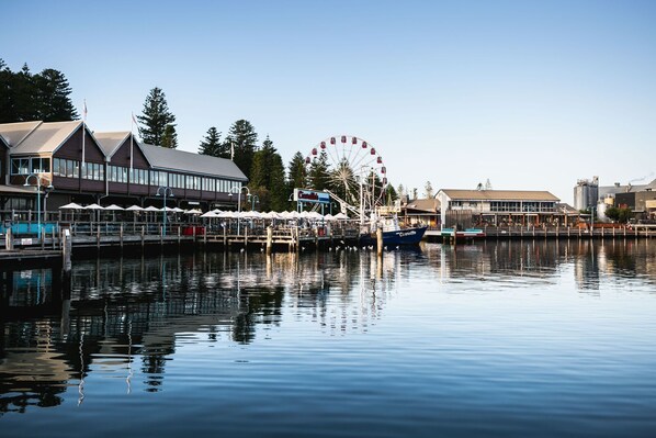A waterfront area with a Ferris wheel, a dock with boats, and buildings with outdoor seating. - Oceanside 8 beach (Fremantle)
