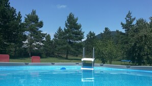 Una piscina de blau clar amb un videt de rajola, envoltada d'arbres i una zona verda.