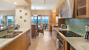 A kitchen with a view of the ocean, stainless steel appliances, and a dining area with wicker chairs. - Land`s End Beachfront Elegance: Top Floor Corner (Treasure Island)