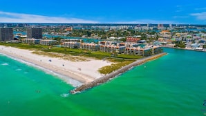 An aerial view of a coastal resort with beachfront properties, a sandy beach, and a clear blue sky. - Land`s End Beachfront Elegance: Top Floor Corner (Treasure Island)