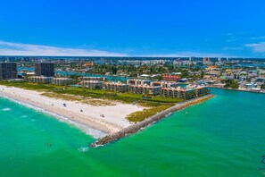 An aerial view of a coastal resort with beachfront properties, a sandy beach, and a clear blue sky.