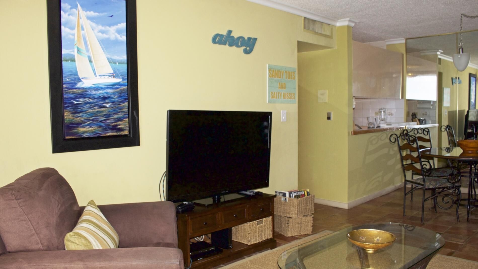 A living room with a sofa, a television, a glass coffee table, and a painting of a sailboat.