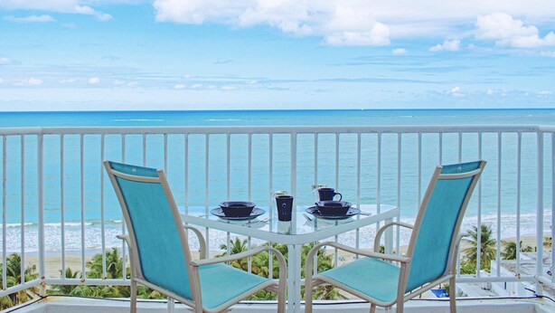 Un balcón con dos sillas y una mesa, con vista a una playa y al océano.