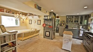 A kitchen with a refrigerator, stove, and cabinets. There is a dining table with chairs and a bookshelf.