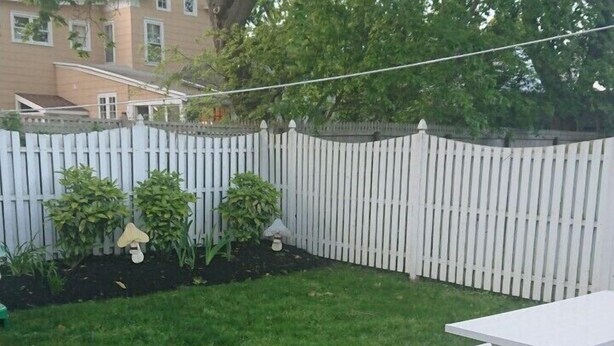 A backyard with a white fence, a grassy lawn, and a white picnic table.