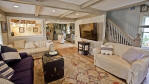A spacious living room with a large sofa, a smaller sofa, and a coffee table. There is a staircase leading to another level, and a kitchen area is visible in the background.