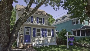 A two-story house with a front porch, a mailbox, and a sign indicating a cottage.