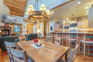 A spacious living area with a wooden dining table, chairs, a fireplace, and a kitchen area with wooden cabinets and a refrigerator.