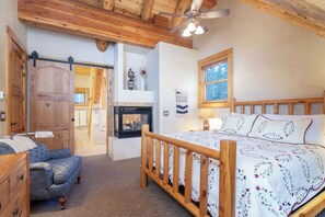 A bedroom with a wooden bed, a nightstand, a dresser, a fireplace, and a ceiling fan.