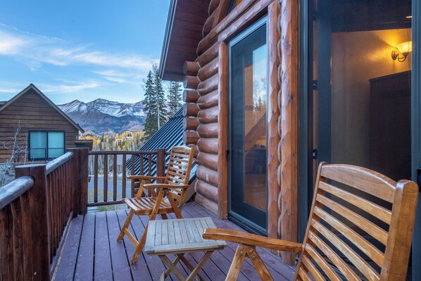 Mountain View Estates 2 Uncovered Terrace - Telluride - A small wood deck with two folding chairs and a side table by a sliding glass door, with snowy peaks beyond. The uncovered terrace is shared by Bedrooms 3 and 4 in this Telluride home.