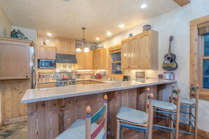 A kitchen with wooden cabinets, a central island with bar stools, a stove, and a microwave.