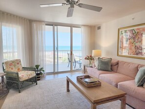 A living room with a sofa, a chair, a coffee table, and a view of the ocean through a sliding glass door.