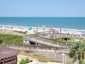 A wooden boardwalk leading to a beach with umbrellas and people. - Cambridge 302 Beautiful Views from Large Oceanfront Balcony (Pawleys Island)