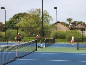 A tennis court with a net, surrounded by a fence and trees.