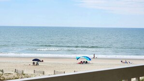 A beach with a clear sky, calm sea, and a few people and dogs. - Cambridge 302 Beautiful Views from Large Oceanfront Balcony (Pawleys Island)