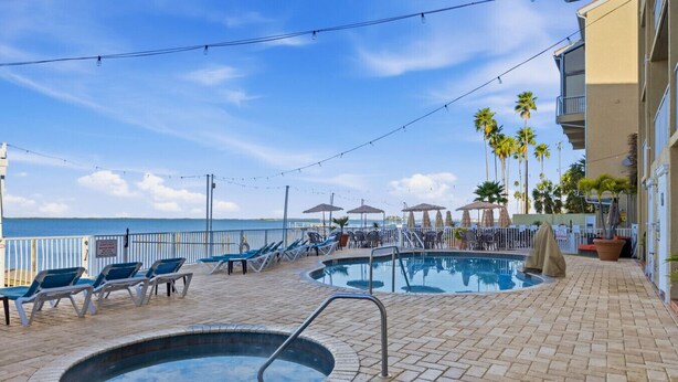 A pool area with lounge chairs and umbrellas, a pool, and a view of the ocean. - Waterfront Studio at Beso del Sol | Pool, Balcony, Sunset Bar (Dunedin)
