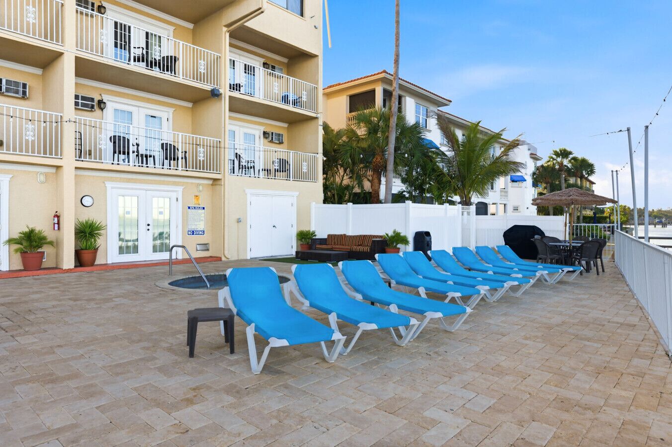 A hotel with a pool area featuring blue lounge chairs, a barbecue, and a dining area.