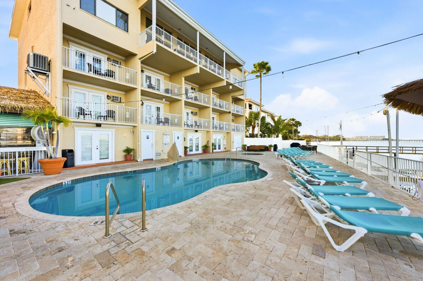 A swimming pool with lounge chairs, a building with balconies, and a palm tree.