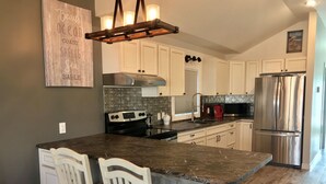 A modern kitchen with white cabinets, a granite countertop, a stainless steel refrigerator, and a built-in stove.