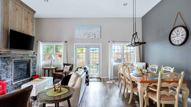 A modern living room with a fireplace, a dining area with wooden chairs, and a large clock on the wall.