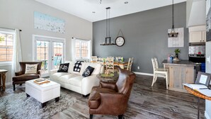 A spacious living room with a white sofa, a brown leather chair, and a dining area with a wooden table and chairs.