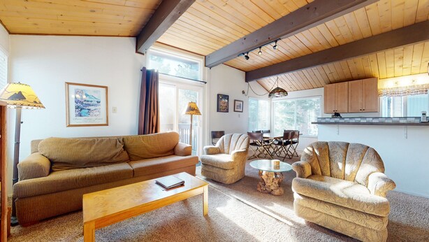 Una sala de estar acogedora con techo de madera, un sofá, sillones, una mesa de centro y un comedor con mesa y sillas.