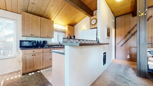 Una cocina con armarios de madera, microondas, cafetera y un reloj en la pared.
