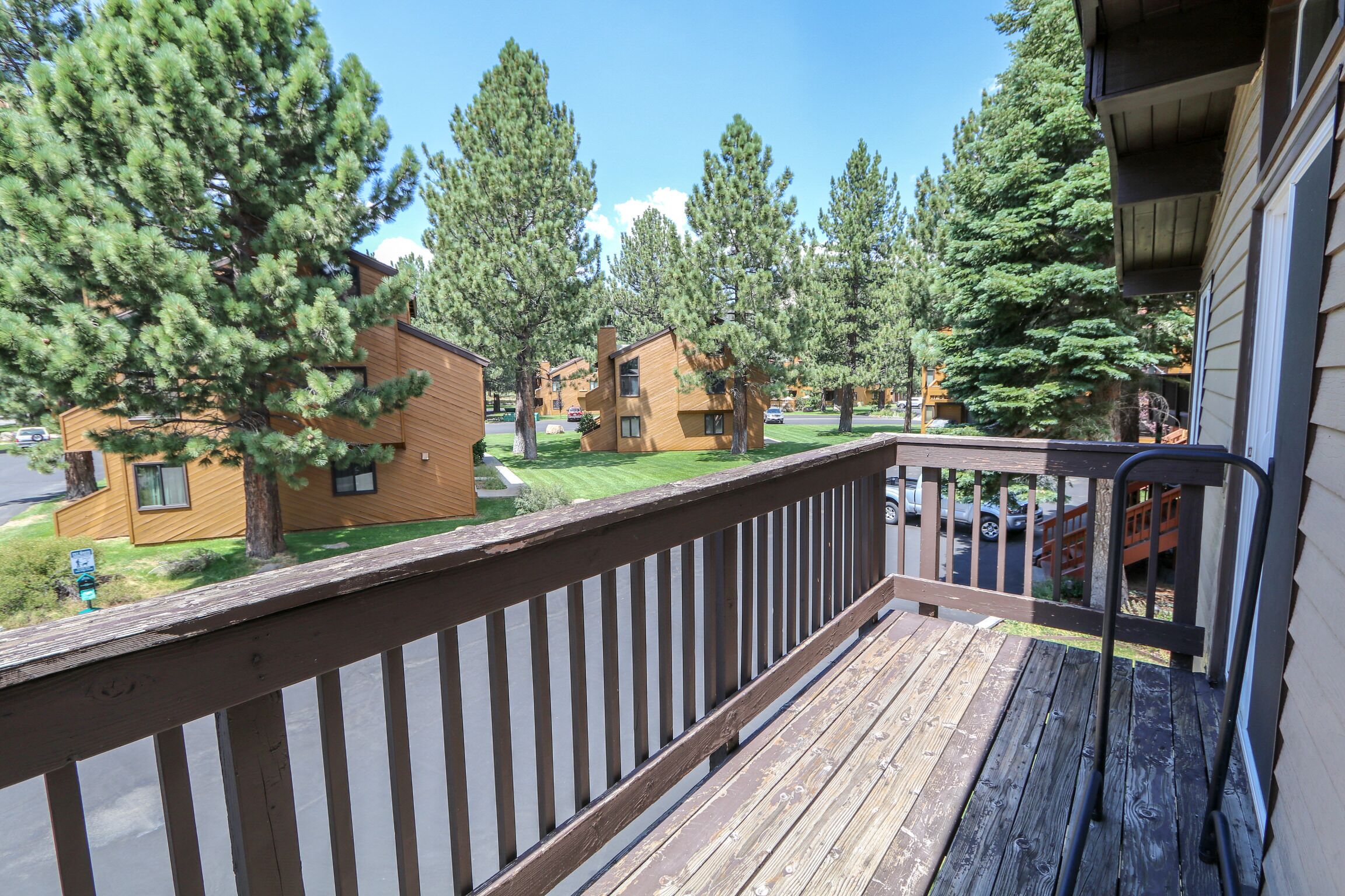 A wooden deck with a railing, overlooking a residential area with multiple houses and tall trees.