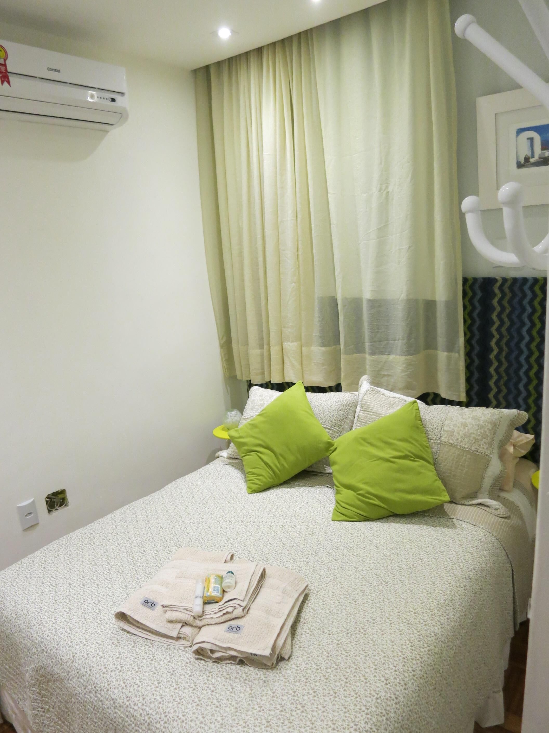 Una cama bien hecha con almohadas verdes, una toalla doblada y artículos de aseo sobre la cama.