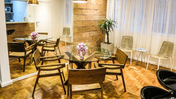 Un espace repas moderne avec une table en verre entourée de chaises en bois, un mur décoratif en briques et une plante en pot.