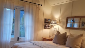A bedroom with a large bed, a window with curtains, a lamp, and a small table.
