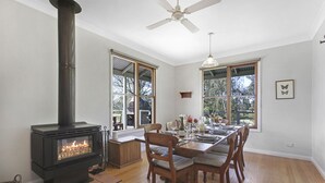 Ein Essbereich mit Kaminofen, großen Fenstern und Deckenventilator.