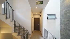 Um corredor com uma escada à esquerda, uma porta no final e uma janela à direita.