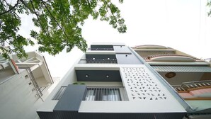 Um edifício de vários andares com varandas, fachada geométrica e uma árvore em primeiro plano.