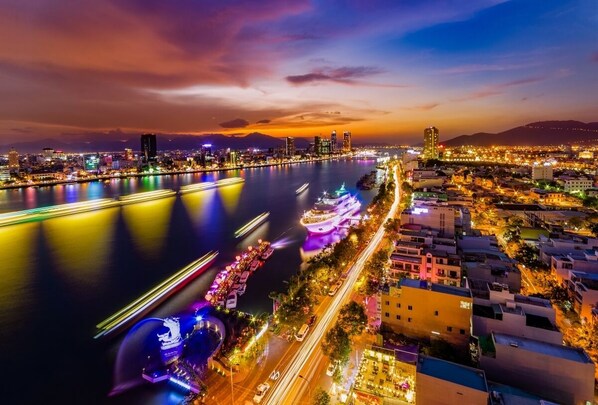 A nighttime cityscape with a river, illuminated buildings, and a bridge.