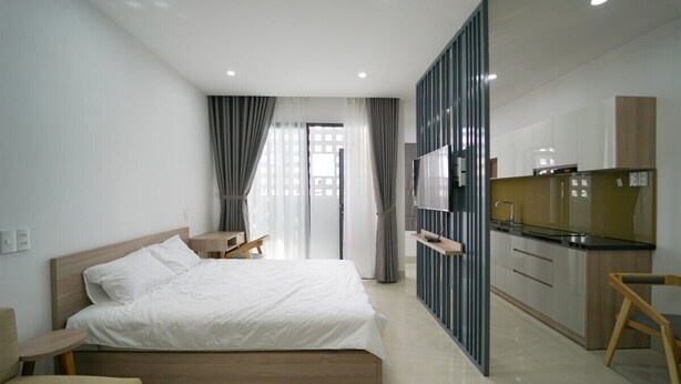 Quarto de hotel moderno com uma cama grande, uma escrivaninha, uma TV e uma cozinha compacta.