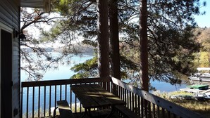 Eine Holzterrasse mit Picknicktisch und Bänken mit Blick auf einen See, umgeben von hohen Bäumen.